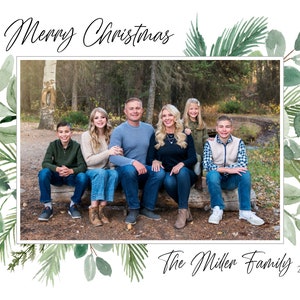 May include: A Christmas card featuring a family of six posing in a forest setting. The card has a green watercolor border with leaves and branches. The text "Merry Christmas" is at the top of the card and "The Miller Family 2021" is at the bottom.