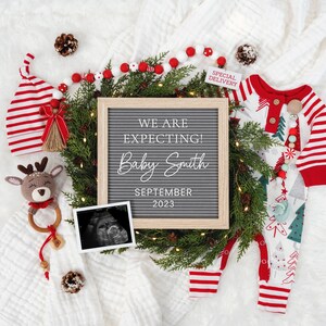 May include: A Christmas-themed pregnancy announcement with a letter board that reads "We are expecting! Baby Smith September 2023". The letter board is surrounded by a wreath of evergreen branches, red and white striped stockings, a baby onesie, and a small stuffed reindeer.