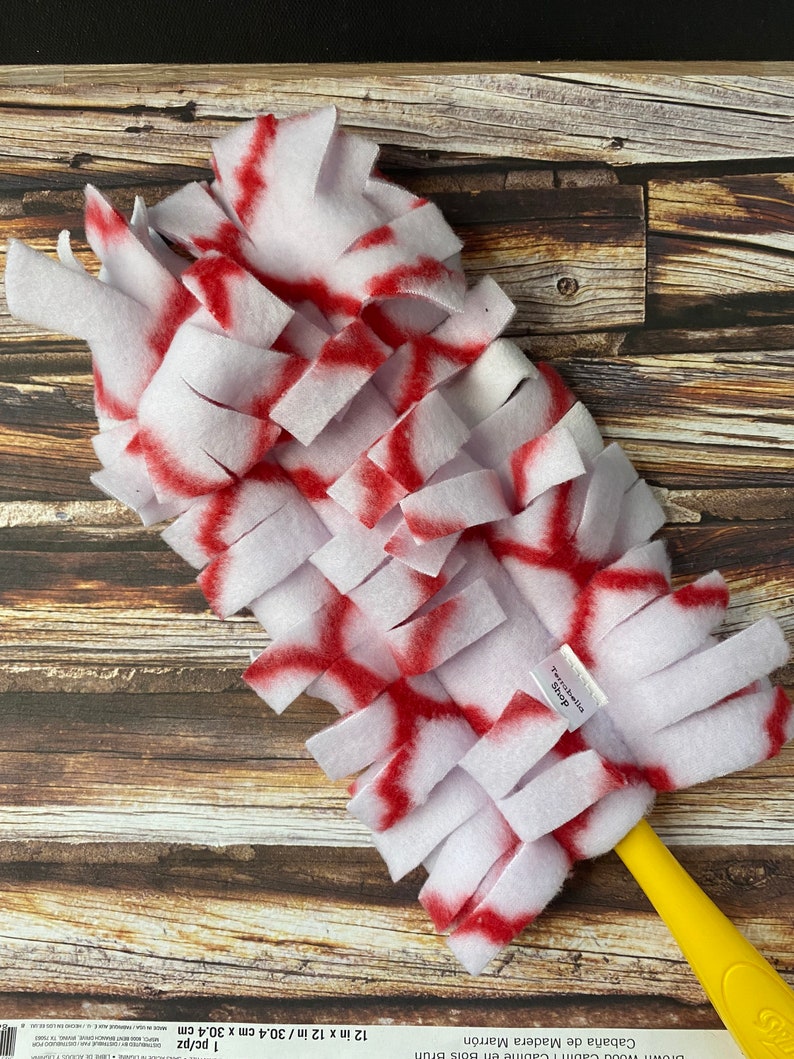 May include: White and red dog toy with a yellow handle. The toy is made of soft, fuzzy material and is designed to be interactive for dogs.