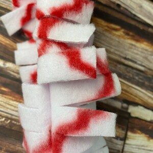May include: A white and red fabric strip with frayed edges. The fabric is cut into strips and sewn together to create a fluffy texture.