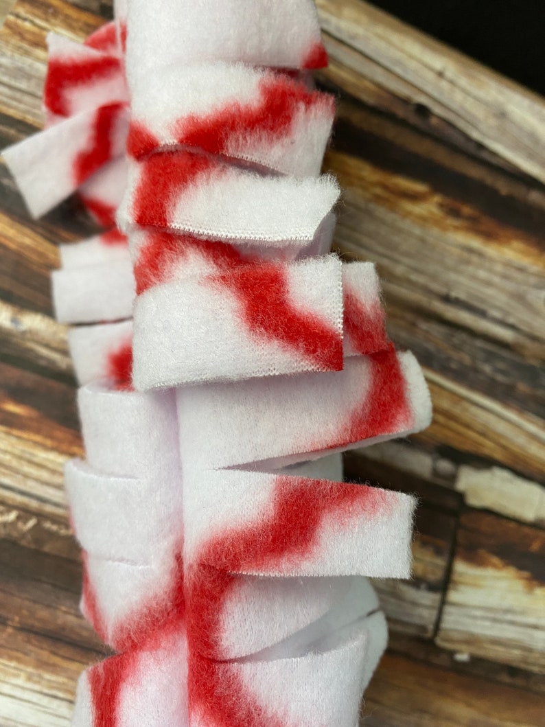 May include: A white and red fabric strip with frayed edges. The fabric is cut into strips and sewn together to create a fluffy texture.