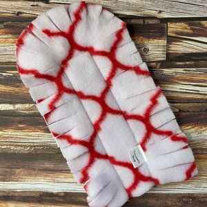May include: White and red fleece dog toy with a fringe border. The toy has a geometric pattern and the text "Tenabella Shop" is printed on the toy.