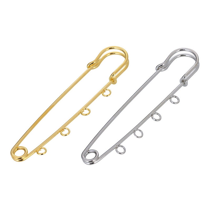 May include: Two safety pins with loops. One is gold and the other is silver.