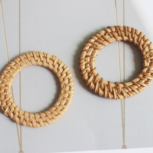 May include: Two woven rattan hoops, one slightly larger than the other, with a natural brown color. The hoops are made of thin, interwoven strands of rattan.
