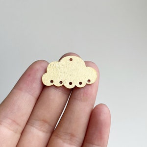 Könnte beinhalten: Ein goldfarbener Holz-Wolkenanhänger mit gewelltem Rand und sechs Löchern. Der Anhänger ist etwa 5 cm breit.