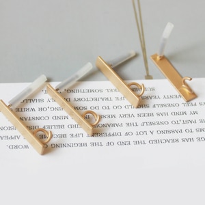 May include: Four gold-colored bar earrings with a small loop at the bottom and a post for insertion. The earrings are rectangular and have a matte finish. The background is a white surface with printed text.
