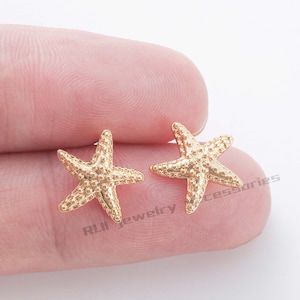 May include: A pair of gold-tone starfish stud earrings. The earrings are small and delicate, and they have a textured surface.