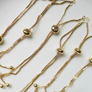 May include: A set of six gold-toned adjustable bracelet chains with round beads. Each chain has two strands and a sliding bead for adjusting the length.