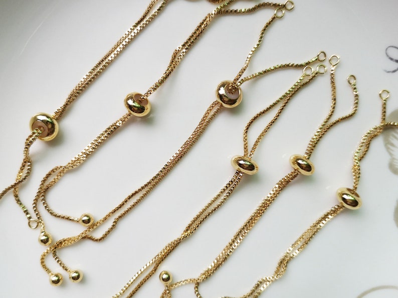 May include: A set of six gold-toned adjustable bracelet chains with round beads. Each chain has two strands and a sliding bead for adjusting the length.