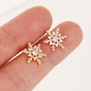 May include: Two gold-tone snowflake charms with clear crystal accents. Each charm has a loop for attaching to jewelry or other crafts.