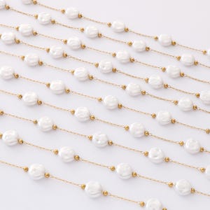 May include: A long gold chain necklace with white pearl-like beads. The chain is made of small gold links and the beads are round and slightly irregular in shape.
