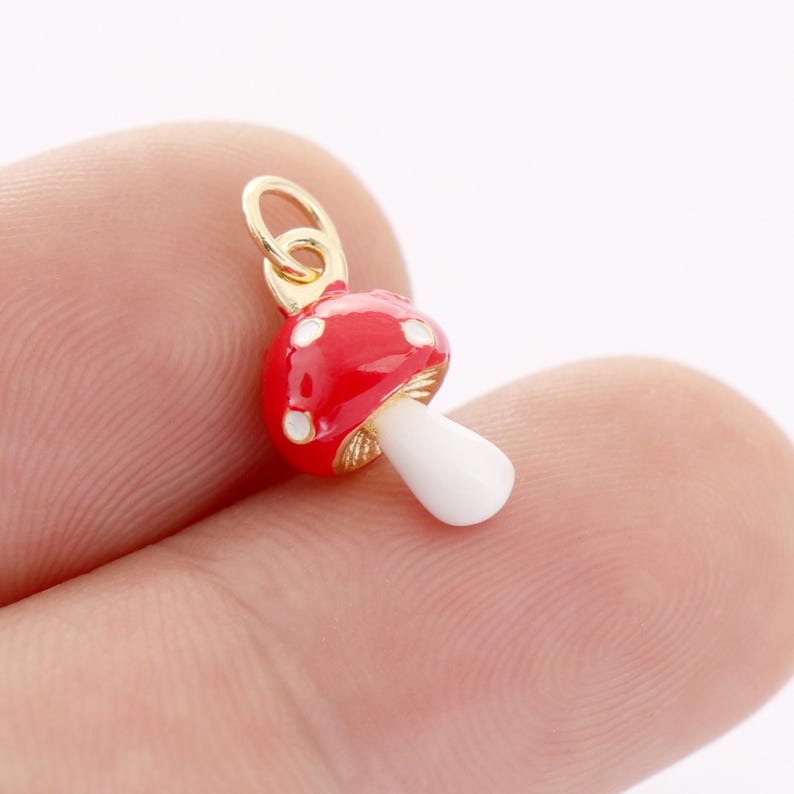 May include: A gold charm shaped like a red and white mushroom with white spots. The charm is ideal for adding a whimsical touch to jewellery.