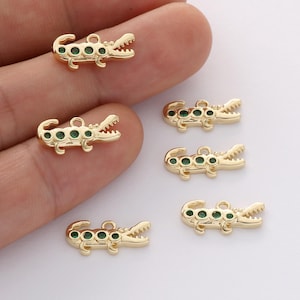 Könnte beinhalten: Goldfarbene Alligator-Anhänger mit grünen Akzenten. Die Anhänger zeigen ein detailliertes Alligatordesign mit offenem Maul und kleinen grünen Edelsteinen. Ideal für Schmuckherstellung oder Bastelprojekte.