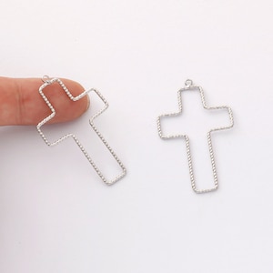 May include: Two silver metal cross shapes with a textured rope design. The crosses have a loop at the top for hanging.
