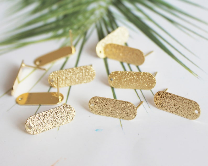 May include: A close-up of eight gold-toned oval-shaped earring blanks with textured surfaces. The earring blanks have a small hole at the top and a post on the back.