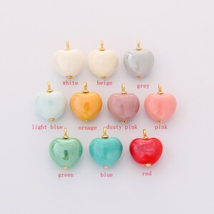 Peut inclure: Une collection de pendentifs en forme de cœur de différentes couleurs : blanc, beige, gris, bleu clair, orange, rose poudré, rose, vert, bleu et rouge. Chaque pendentif a une bélière dorée pour l'attacher.