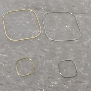 Può includere: Quattro braccialetti quadrati in oro e argento. Sono presentati due braccialetti più grandi e due più piccoli. I braccialetti hanno angoli arrotondati e un design minimalista.