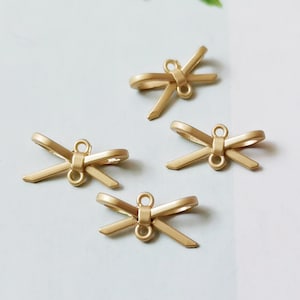 May include: Four gold-colored metal bow charms with a loop at the top for attaching to jewelry or other crafts.