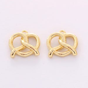 May include: Two gold-colored metal charms shaped like pretzels. The charms have a hole at the top for attaching to jewelry or other crafts.