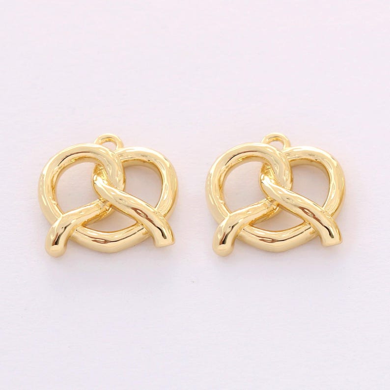 May include: Two gold-colored metal charms shaped like pretzels. The charms have a hole at the top for attaching to jewelry or other crafts.