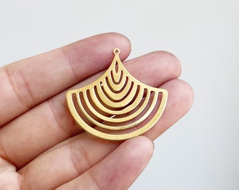Può includere: Un ciondolo in metallo dorato con un design geometrico. Il ciondolo ha una forma a ventaglio con più cerchi concentrici. Ha un piccolo anello nella parte superiore per attaccare una catena o un cordino.