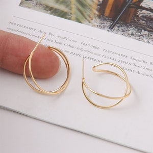 Könnte beinhalten: Ein Paar goldene Creolen mit einem doppelschichtigen Design. Die Ohrringe sind aus dünnem Metall gefertigt und haben einen schlichten, modernen Stil.