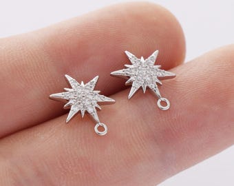 May include: Two silver-colored star-shaped earring charms. Each charm features a starburst design with multiple points and a central cluster of small, clear stones. A small loop is attached to each charm for easy attachment to earring hooks.