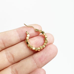 May include: Gold hoop earrings made of small, square-shaped beads.