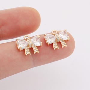 May include: Two gold-tone bow charms with clear crystal accents. The charms have a loop at the top for attaching to jewelry or other crafts.