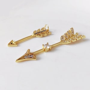 May include: Two gold arrow charms with clear and blue crystals. The arrowheads are adorned with clear crystals, while the feathers are embellished with clear and blue crystals.