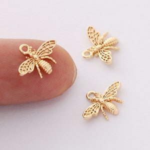 May include: Three gold bee charms with a detailed design. The charms have a loop at the top for attaching to jewelry or other crafts.