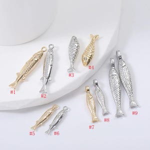 May include: Nine metal fish charms in gold and silver. The charms have different designs, some with textured scales and others smooth. Each charm has a loop for attaching to jewellery. Measurements are in centimetres.