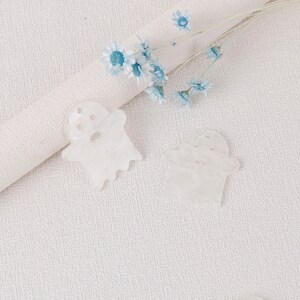 Puede incluir: Dos decoraciones blancas en forma de fantasma sobre un fondo blanco texturizado con un ramo de flores azules.