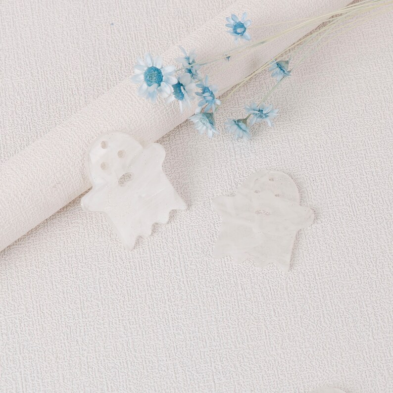 Puede incluir: Dos decoraciones blancas en forma de fantasma sobre un fondo blanco texturizado con un ramo de flores azules.