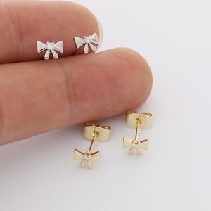 Peut inclure: Deux paires de boucles d'oreilles à tige en forme de nœud. Une paire est en métal argenté et l'autre en métal doré. Chaque nœud comporte une petite pierre précieuse ronde et transparente sertie au centre. Les boucles incluent des fermoirs à tige.