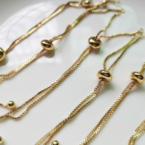 May include: Four gold chain bracelets with adjustable sliding beads. Each bracelet has two chains and a round bead at the end of each chain.