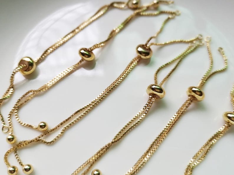 May include: Four gold chain bracelets with adjustable sliding beads. Each bracelet has two chains and a round bead at the end of each chain.