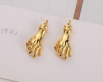 May include: Two gold-toned hand charms with a detailed design. The hands are in a gesture of holding something.