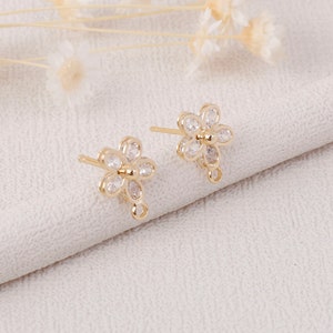 May include: Two gold-tone flower-shaped earring findings with clear cubic zirconia stones. Each finding has a loop for attaching a dangle charm.
