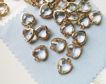 May include: A collection of gold-toned heart-shaped charms with clear crystal accents. The charms have a loop at the top for attaching to jewelry or other crafts.