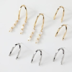 May include: A set of three pairs of earrings. Two pairs are gold with a curved design and a dangling row of white beads. The third pair is silver with a curved design.