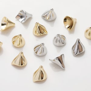May include: A collection of gold and silver metal cone-shaped beads with a ruffled texture. The beads are scattered on a white surface.