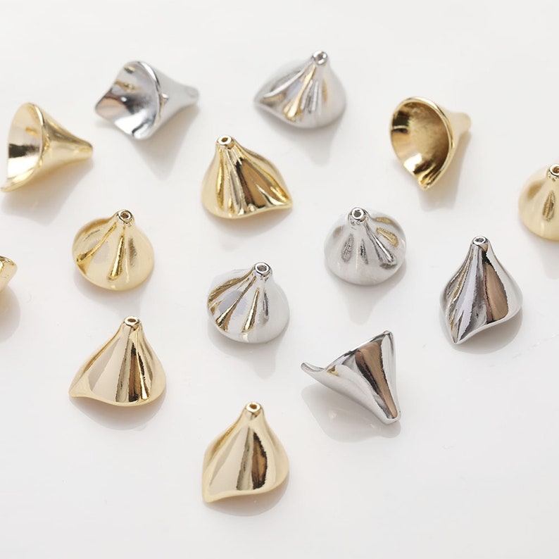 Peut inclure: Un ensemble de perles en m&eacute;tal de couleur or et argent de forme conique avec une texture pliss&eacute;e. Les perles sont &eacute;parpill&eacute;es sur une surface blanche.