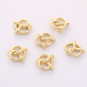 May include: Six gold-toned metal charms shaped like pretzels. The charms have a loop at the top for attaching to jewelry or other crafts.
