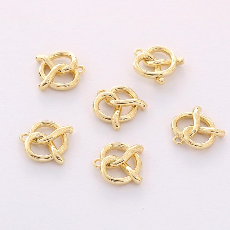 May include: Six gold-toned metal charms shaped like pretzels. The charms have a loop at the top for attaching to jewelry or other crafts.