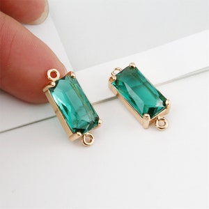 May include: Two gold-toned connector charms with emerald green rectangular glass stones. The charms have two loops on each side for attaching to jewelry.