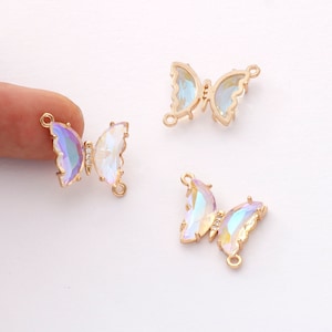 May include: Three iridescent butterfly charms with gold-colored frames. The butterfly wings have a shimmering, multi-colored effect. One charm is held by a finger. Each charm has a small loop for attaching to jewelry.