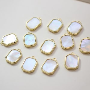 May include: Ten gold-toned pendants with a white iridescent shell inlay. Each pendant is shaped like a rectangle with rounded corners and has a small loop at the top for attaching to a chain or cord.