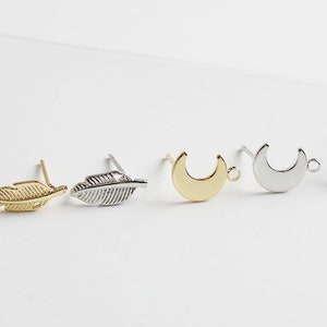 Puede incluir: Cuatro hallazgos de pendientes con diferentes formas: una pluma dorada, una pluma plateada, una luna creciente dorada y una luna creciente plateada.
