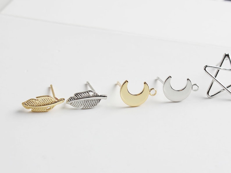 Puede incluir: Cuatro hallazgos de pendientes con diferentes formas: una pluma dorada, una pluma plateada, una luna creciente dorada y una luna creciente plateada.